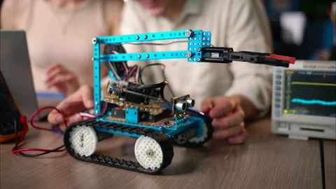 Two young happy engineers fixing a mechanical robot car in the workshop, Stock Footage 247476004