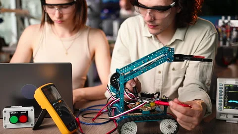Two young happy engineers fixing a mechanical robot car in the workshop, Stock Footage 247476144