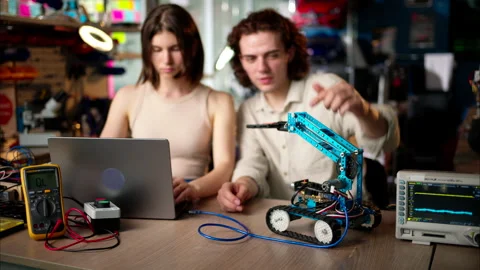 Two young happy engineers fixing a mechanical robot car in the workshop, Stock Footage 247486514