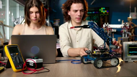 Two young happy engineers fixing a mechanical robot car in the workshop, Stock Footage 247486773