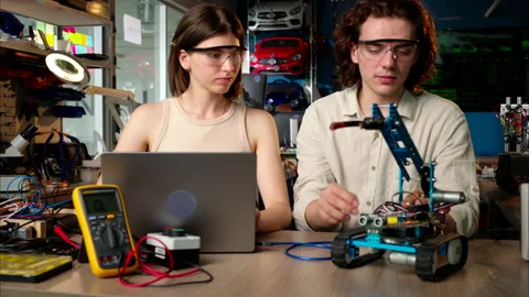 Two young happy engineers fixing a mechanical robot car in the workshop, Stock Footage 247493685