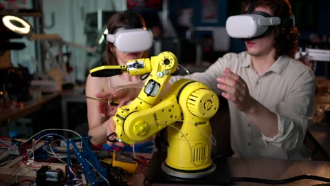 Two young happy engineers with VR virtual reality headsets fixing an yellow Stock Footage 247420071