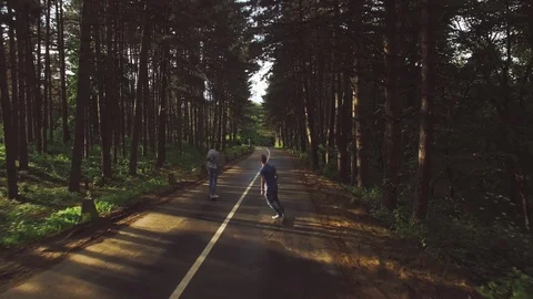 Two young hipster man riding longboards on a pavement road through the forest. Stock Footage 125641266