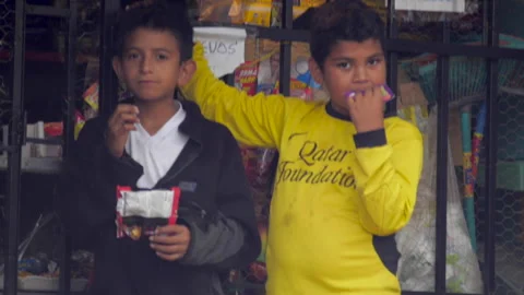 Two young Hispanic boys eating junk food in front of a small neighborhood store Stock Footage 146013393