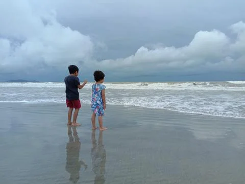 Two young kid playing by the beach, by the wave edge, with cloudy sky Stock Photos