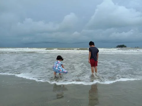 Two young kid playing by the beach, by the wave edge, with cloudy sky Stock Photos