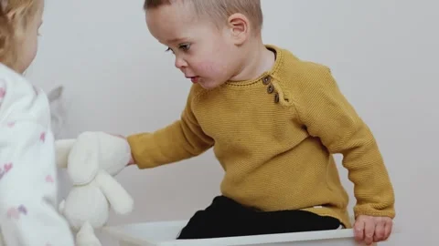 Two young kids are having fun indoors. One child sits in a plastic bin while the Stock Footage 336460288