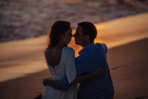 Two young lovers standing on a beach and looking to each other on sunset Stock Photos