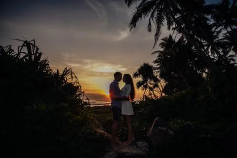 Two young lovers standing on a beach and looking to each other on sunset palm Stockfoto's
