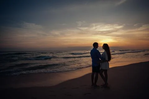 Two young lovers standing on a beach and looking to each other on sunset Stock Photos