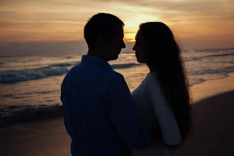 Two young lovers standing on a beach and looking to each other on sunset Stock Photos