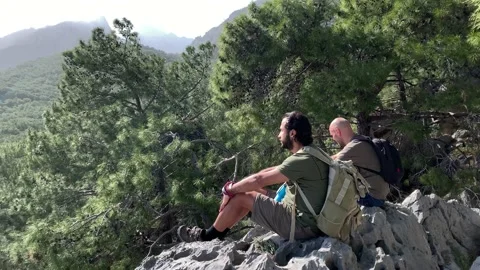 Two young man multi cultural sitting at cliff looking at Mediterranean Sea Stock Footage 149471644