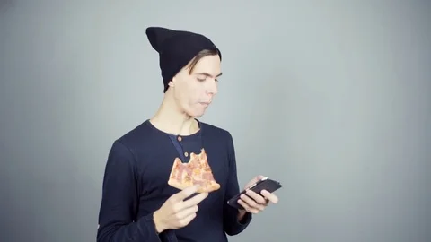 Two young man in studio eating pizza using smartphone drinking coffee gray Stock Footage 70260972