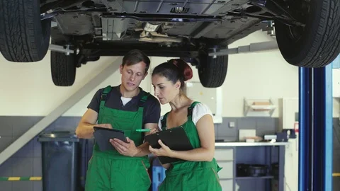 Two young mechanics of a guy and a girl are reading from the tablet a diagram Stock Footage 94655547