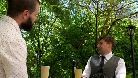 Two young men are sitting in a cafe on the street. They drink coffee. Stock Footage 89268922