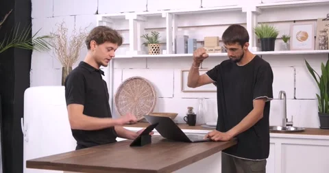 Two young men are using a digital tablet and laptop in the kitchen Stock Footage 247472197