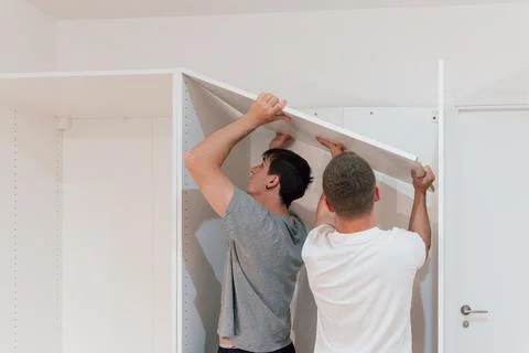 Two young men assembling a closet shelf in a new apartment. Furniture Concept Stock Photos