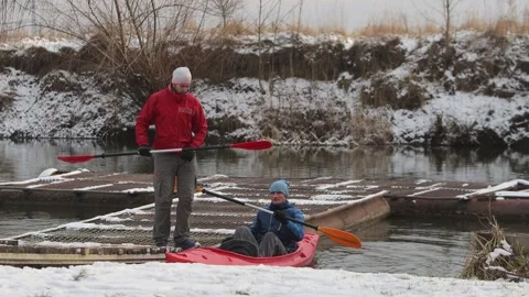 Two young men of athletic build sit in a red kayak. Winter scene. Video stock 299710739