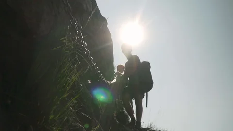 Two young men climbing down rocks while holding a chain with sun flare Stock Footage 129611945