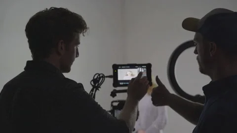 Two young men consulting footage on set, film crew working behind camera Stock Footage 208714740