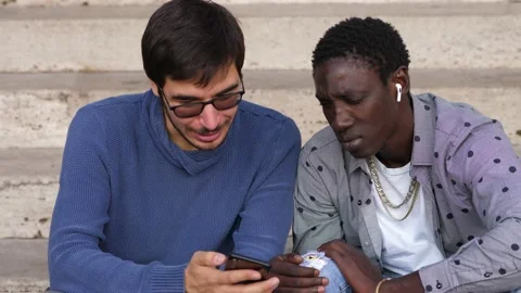 Two young men of different ethnicities are looking at a photo on mobile phone Stock Footage 231693216