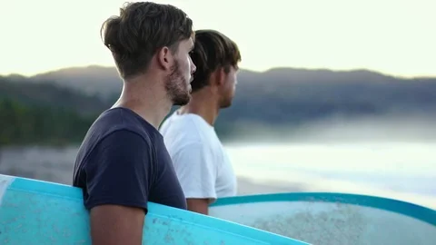 Two young men friends on beach with surfboards at sunrise.  Stock Footage 108564204