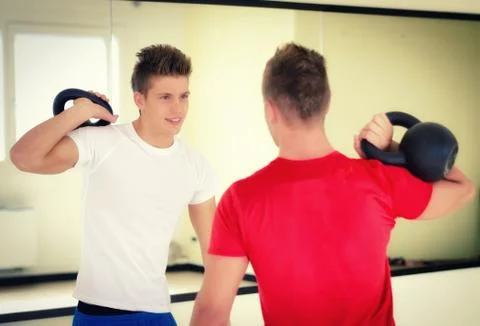 Two young men in gym working out with kettlebells Stock Photos
