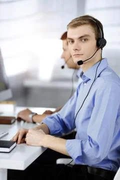 Two young men in headset, sitting at the desk in a sunny modern office 库存照片