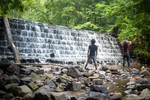 Two young men hike to the base of a waterfall. Stock Photos