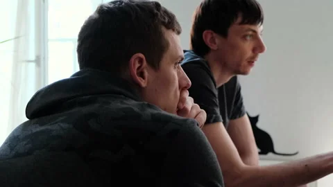 Two young men looking in the same direction and communicate sitting at home 動画素材 136888641