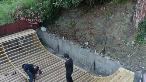 Two young men making a skate ramp in backyard. Tilt down reveal shot. Video stock 159791191