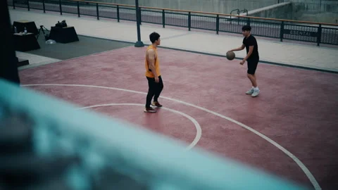 Two young men play basketball on a red outdoor court with white lines, one Stockbeeldmateriaal 347333473