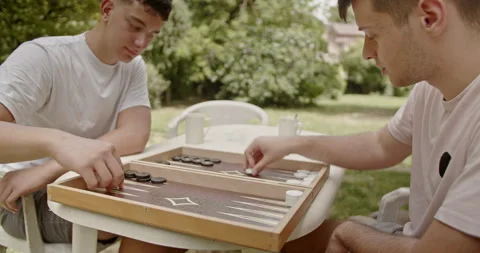 Two young men play a game of backgammon at an outdoor table surrounded by Stockbeeldmateriaal 281580830