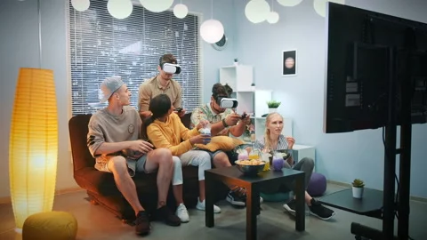 Two young men playing console game in virtual reality glasses among cheerful Stock Footage 157645647