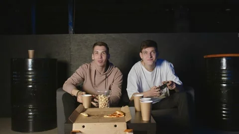 Two young men playing video game, sitting at couch in dark room Stock Footage 136339314