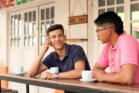 Two young men relax drinking coffee and talking in an urban latin locale. Fotos de archivo