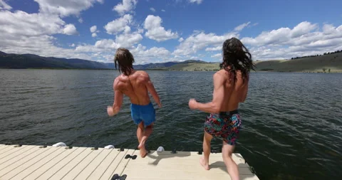 Two young men running off dock back flipping into lake Stock Footage