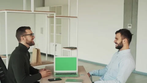 Two young men shake hands in the office on the background of a laptop with Stock Footage 228683511