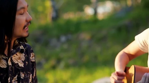 Two young men singing, playing guitar and spending weekend outdoors in the Stock Footage 76010582