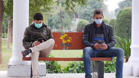 Two young men sitting on a bench in a park keeping social distance Stock Photos