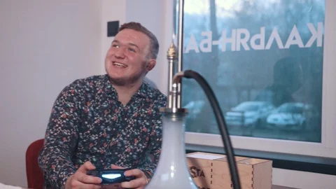 Two young men sitting in cafe at table playing game console and Smoking a hookah Stock-Footage 117700593