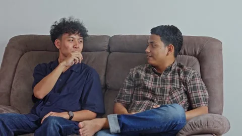 Two young men sitting laughing and talking while one uses vape device exhaling Stock Footage 332751171