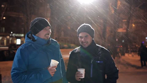 Two young men stand on the street in winter, heavy snow, chatting and drinking Stock Footage 101716603