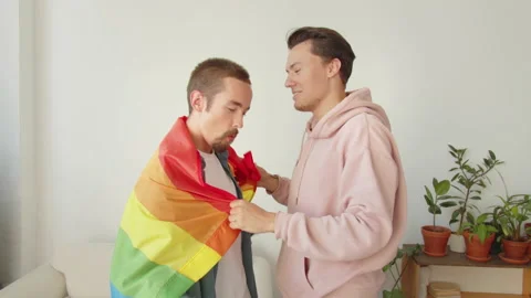 Two young men stand together, covered with a lgbt flag, and dance a little Stock Footage 174448812