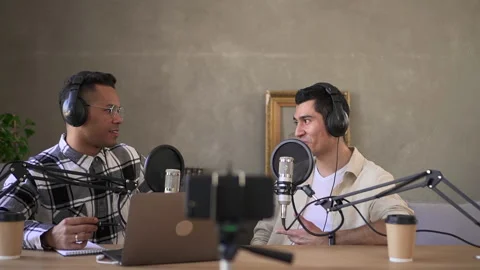 Two young men talking and recording audio podcast while sitting at table in Stock Footage 167320281