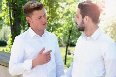 Two young men talking to each other in park Stock Photos