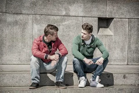 Two young men talking while sitting on curb Stock Photos