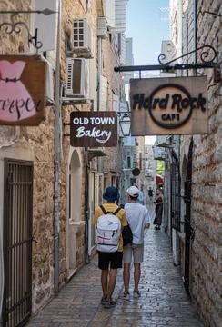 Two young men walk away from the camera down a narrow, cobblestone alley Stock Photos