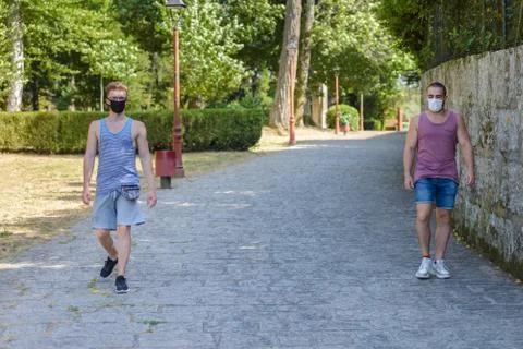 Two young men walk down the street wearing medical masks on their faces, keep Stock Photos