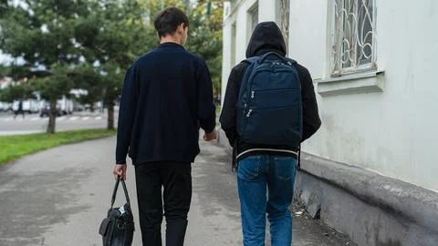 Two young men walk down a sidewalk in an urban area on a cloudy day, sharin.. Stock Photos